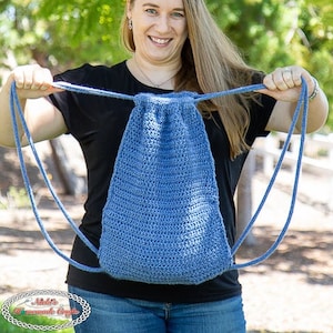 May include: A woman is holding a blue crocheted drawstring bag with long straps. The bag is made with a textured stitch pattern.