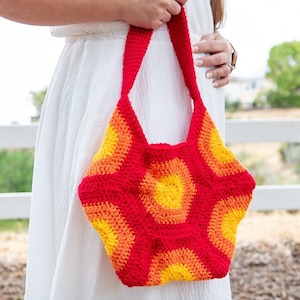 Könnte beinhalten: Eine rote, orange und gelbe gehäkelte Tragetasche mit geometrischem Muster. Die Tasche hat einen einzigen Riemen und wird über der Schulter getragen.