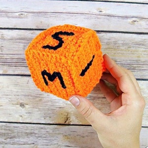 May include: A crocheted orange cube with black letters spelling out "SMI" on the visible sides.
