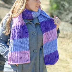 May include: A woman wearing a gray coat with a purple, pink, and blue striped crocheted scarf.