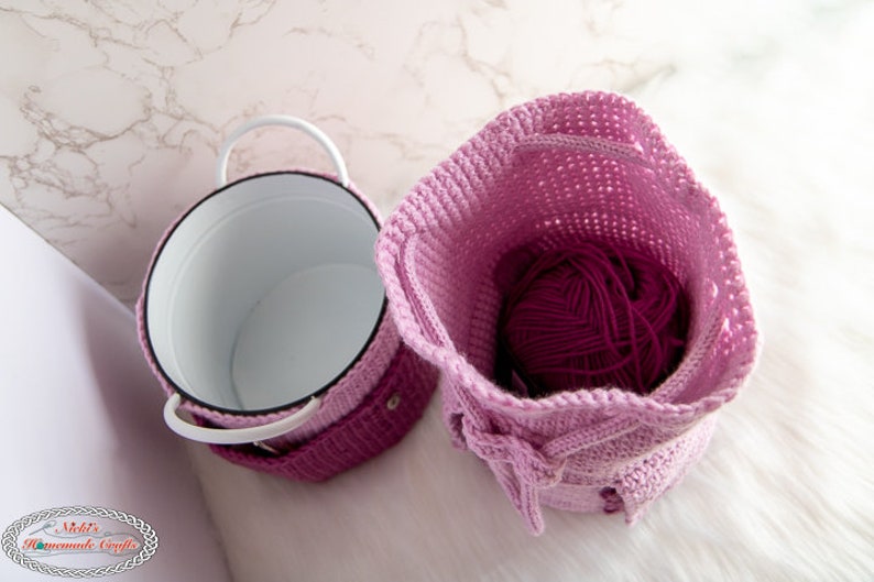 Puede incluir: Dos cestas de almacenamiento de crochet, una rosa y otra morada, con un contenedor de metal blanco dentro de la cesta rosa. La cesta morada est&aacute; llena de una bola de hilo.
