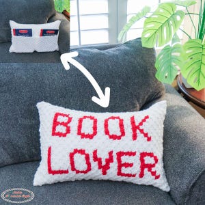 Puede incluir: Un cojín blanco texturizado con las palabras "BOOK LOVER" en rojo. El cojín rectangular está sobre un sofá gris. Una imagen insertada muestra un cojín más pequeño con bolsillos para guardar libros.