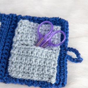 Pu&ograve; includere: Una pochette in crochet blu e grigia con un paio di forbici viola all'interno. La pochette ha un piccolo anello sul lato.