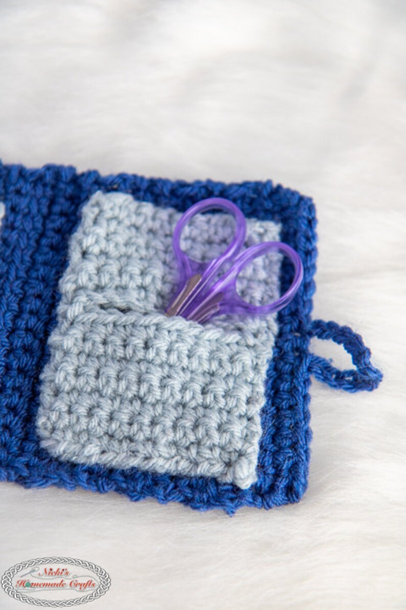 Pu&ograve; includere: Una pochette in crochet blu e grigia con un paio di forbici viola all'interno. La pochette ha un piccolo anello sul lato.