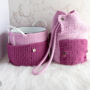 Puede incluir: Dos contenedores de almacenamiento de crochet en tonos rosa y morado. Los contenedores tienen un cierre de cord&oacute;n y un detalle de bot&oacute;n.