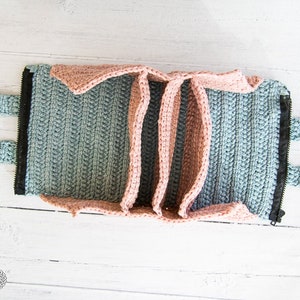Può includere: Una pochette con cerniera a crochet con due manici. La pochette è realizzata in filato blu chiaro e rosa. La cerniera è nera.