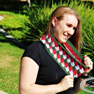 May include: A woman wearing a black top with a green, red and white crocheted cowl neck scarf. The scarf has a chevron pattern.