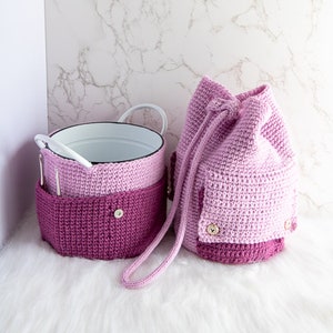 Puede incluir: Dos bolsas de crochet en tonos rosa y morado. Las bolsas tienen un cierre de cord&oacute;n y est&aacute;n hechas con un punto texturizado. Las bolsas est&aacute;n sobre una superficie blanca y esponjosa.