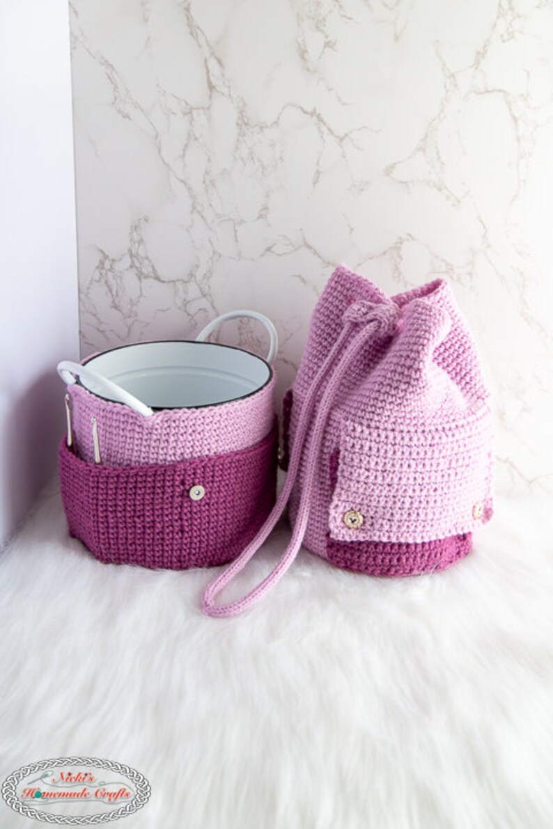 Puede incluir: Dos bolsas de crochet en tonos rosa y morado. Las bolsas tienen un cierre de cord&oacute;n y est&aacute;n hechas con un punto texturizado. Las bolsas est&aacute;n sobre una superficie blanca y esponjosa.
