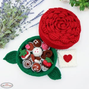 Peut inclure: Un ensemble cadeau fait à la main au crochet. Il comprend une boîte rouge en forme de rose, un plat à bonbons vert avec des chocolats crochetés assortis et une petite enveloppe blanche avec un cœur rouge. Les chocolats incluent des fraises et des truffes.