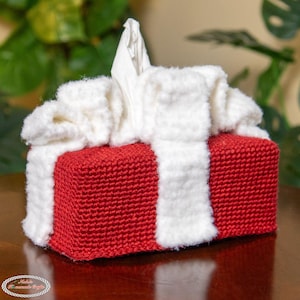 May include: A handmade tissue box cover in red and white. The rectangular box is primarily red, with a textured knit appearance. White, fluffy trim and a white tissue peek out from the top. A decorative item for the home.