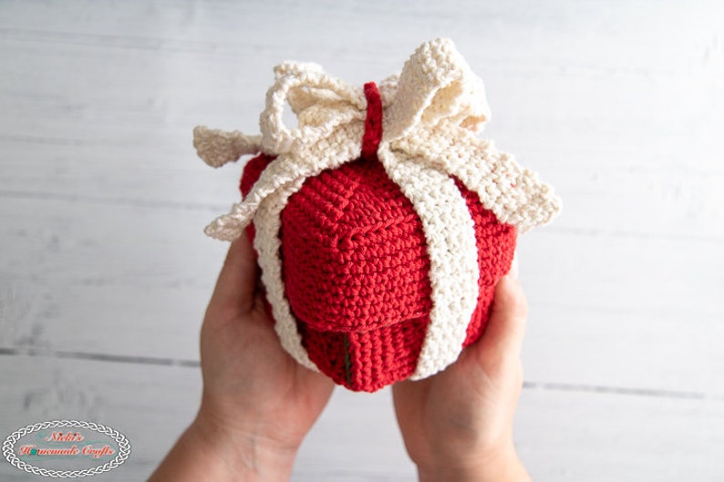 May include: A crocheted red gift box with a white crocheted bow. The box is being held in someone's hands.