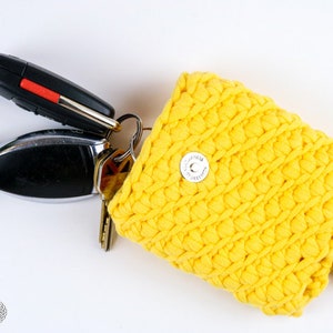 May include: A yellow crocheted key holder with a snap closure. The key holder is filled with keys.