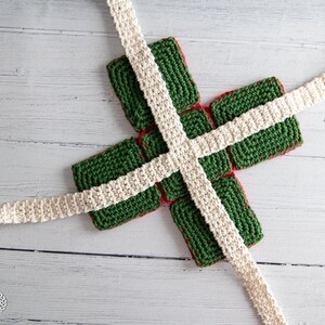 May include: A green and red crocheted gift box with white crocheted ribbon tied around it.
