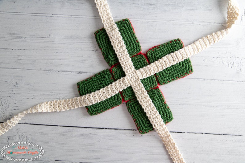 May include: A green and red crocheted gift box with white crocheted ribbon tied around it.