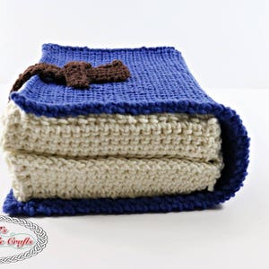 Pode incluir: Um travesseiro de croch&ecirc; em forma de livro com uma capa azul e um marcador de p&aacute;gina de croch&ecirc; marrom. O travesseiro &eacute; feito de duas camadas de tecido de croch&ecirc;, uma branca e uma azul.