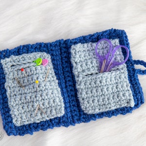 Pu&ograve; includere: Un porta aghi e forbici in crochet blu con due tasche. Il porta aghi ha un bordo blu ed &egrave; aperto per rivelare le tasche. La tasca sinistra contiene diversi aghi da cucito e la tasca destra contiene un paio di forbici viola.
