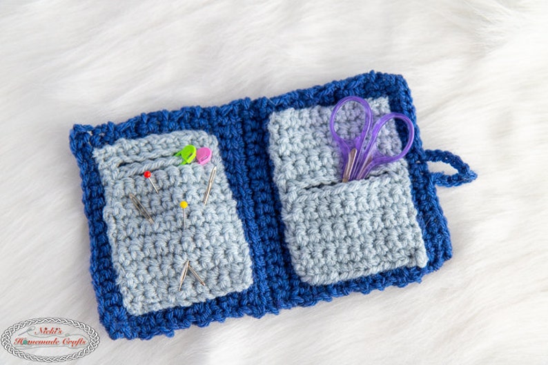Pu&ograve; includere: Un porta aghi e forbici in crochet blu con due tasche. Il porta aghi ha un bordo blu ed &egrave; aperto per rivelare le tasche. La tasca sinistra contiene diversi aghi da cucito e la tasca destra contiene un paio di forbici viola.