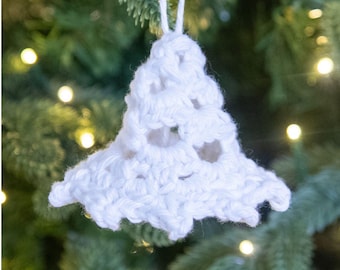 Puede incluir: Adorno navideño de ganchillo blanco hecho a mano con forma de árbol. La decoración en forma de árbol tiene un diseño calado y un lazo para colgar. El adorno se muestra sobre un fondo de un árbol de Navidad con luces suaves y borrosas.