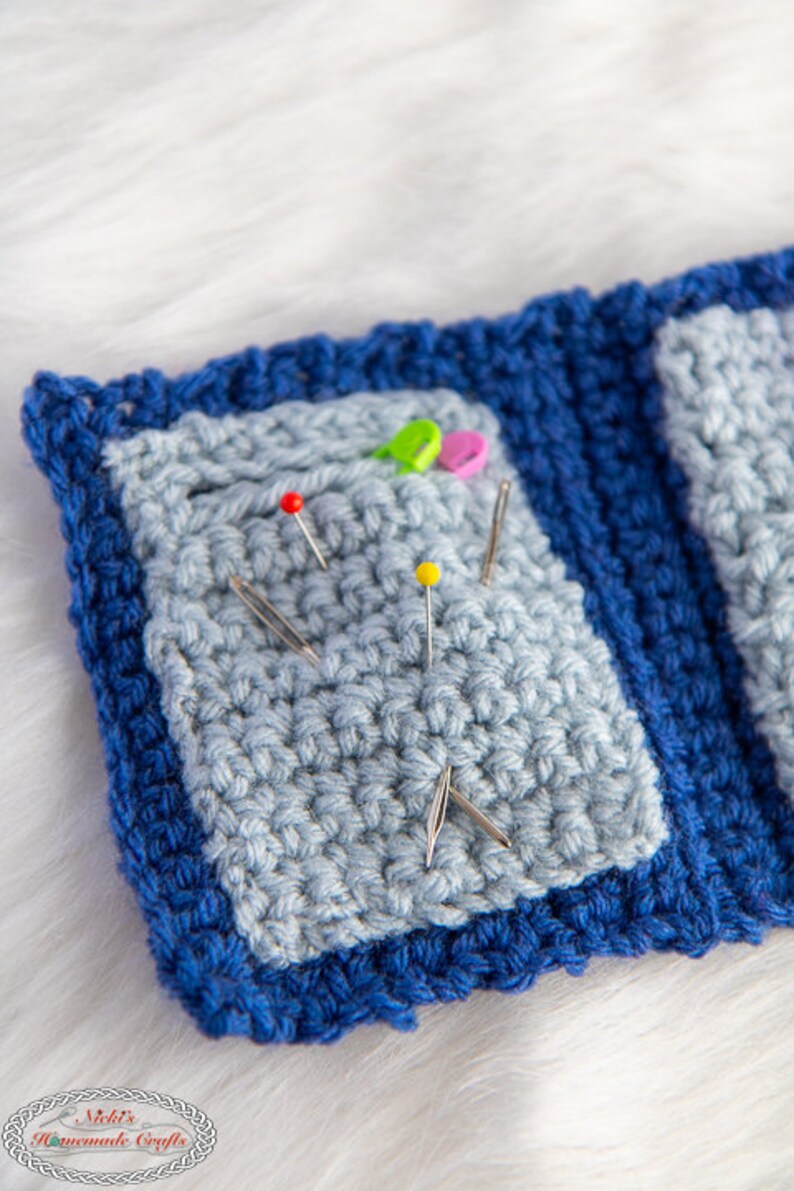 Pu&ograve; includere: Un cuscino per spilli in crochet blu con un centro blu chiaro e una variet&agrave; di spilli e aghi colorati.