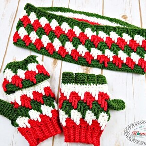 May include: A handmade crochet set in festive colours, including a headband and fingerless gloves. The set is mainly red, white, and green, with a textured, zig-zag pattern. The headband and gloves are displayed on a light wood surface.