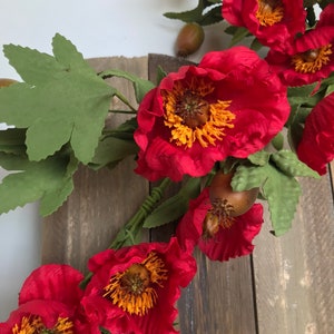 May include: A vibrant floral arrangement featuring large, red peony-like flowers with yellow centers and green leaves. The flowers are set against a rustic wooden background, creating a striking contrast.