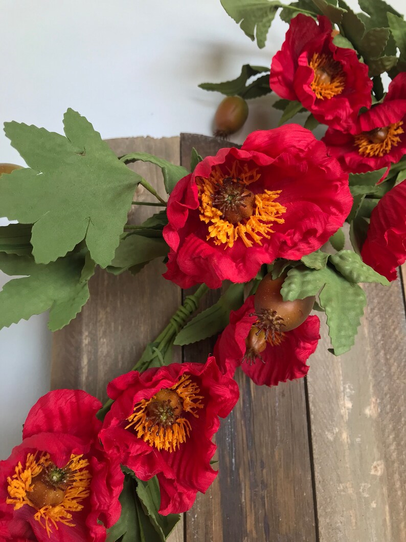 May include: A vibrant floral arrangement featuring large, red peony-like flowers with yellow centers and green leaves. The flowers are set against a rustic wooden background, creating a striking contrast.