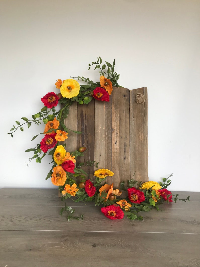 Puede incluir: Un letrero de madera con una guirnalda de flores rojas, naranjas y amarillas. La guirnalda est&aacute; hecha de flores de seda y vegetaci&oacute;n.