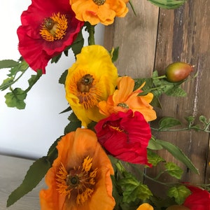 Puede incluir: Una corona floral con flores de amapola rojas, naranjas y amarillas y hojas verdes.
