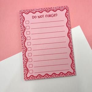 Op de afbeelding: Een rechthoekig notitieblok met een roze luipaardprint rand en een geschulpte rand. Het midden is lichtroze met de tekst DO NOT FORGET: bovenaan, gevolgd door acht horizontale lijnen, elk voorafgegaan door een klein vierkant selectievakje.