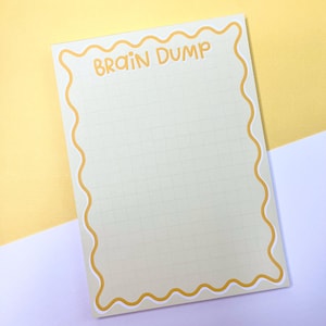 May include: A rectangular notepad with a pale green grid pattern and a wavy yellow border. The text "BRAIN DUMP" is printed in yellow at the top of the page. The notepad features a clean design with a grid layout for writing notes or lists.