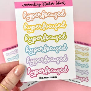 Op de afbeelding: Een vel journaling-stickers met het woord "hyperfocused" in een kleurrijk, handgeschreven lettertype. De stickers zijn in tinten van oranje, geel, groen, blauw, paars en roze. De tekst "Journaling Sticker Sheet" staat bovenaan.