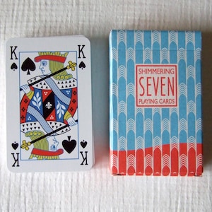 May include: A deck of playing cards with a blue and red design. The box says "Shimmering Seven Playing Cards". The card shown is the King of Spades.