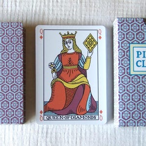 May include: A deck of playing cards featuring a Queen of Diamonds card displayed between the card back and the box. The box and card back have a purple and white hexagonal floral pattern. The box is labeled PIKE CLOVER in a blue rectangle.