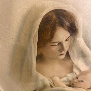 May include: A vintage-style print depicts a woman with brown hair and a white head covering cradling a baby. The baby is fair-skinned with light-colored hair. The artwork has a soft, muted color palette.