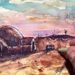 Op de afbeelding: Aquarel schilderij van een woestijnlandschap met koepelvormige structuren en hoge torens onder een zonsonderganghemel. Een hand die een pen vasthoudt, staat op de voorgrond en voegt details toe aan het kunstwerk. De sc&egrave;ne roept een sciencefictionthema op.