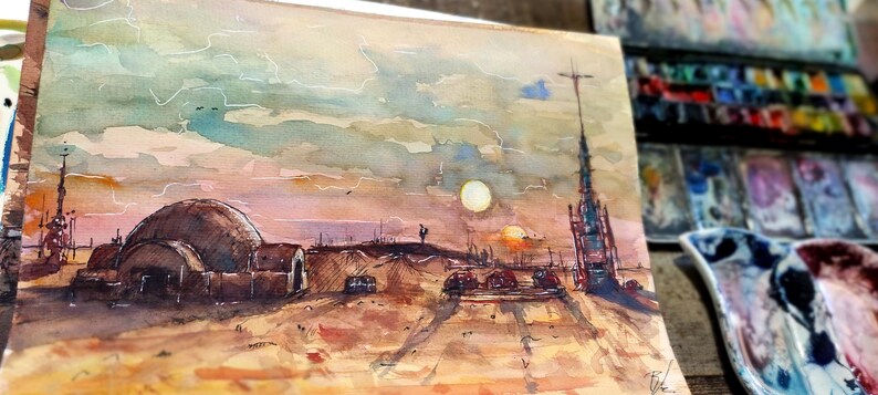 Op de afbeelding: Waterverfschilderij van een woestijnlandschap met een koepelvormige structuur, een hoge toren en ondergaande zonnen. Het kunstwerk gebruikt warme tinten bruin, oranje en geel, met een bewolkte lucht. De schildering is op papier, met een palet en verf op de achtergrond.