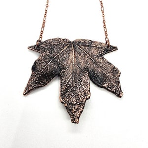 May include: A copper leaf pendant necklace with a detailed, textured design. The pendant is attached to a delicate copper chain.