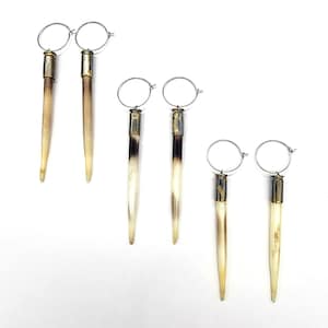Op de afbeelding: Een set van drie paar oorbellen met lange, puntige, bot-achtige hangers met zilveren hoepels en gouden accenten.
