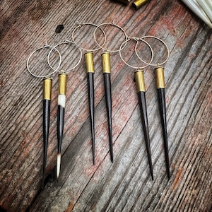 May include: Six pairs of earrings with gold hoops and black and white horn tips. The horn tips are shaped like a point and are attached to a gold bullet casing.