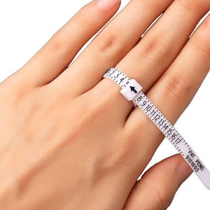 May include: White plastic ring sizer with a numbered scale from 2 to 17. The sizer is wrapped around a finger to determine ring size. The text "PAT. PEND. 9101693" is printed on the sizer.