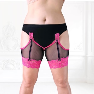 Front-facing image of model in wide stance wearing black mesh anti-chafing thigh bands with pink lace trim. Designed for chub rub protection.