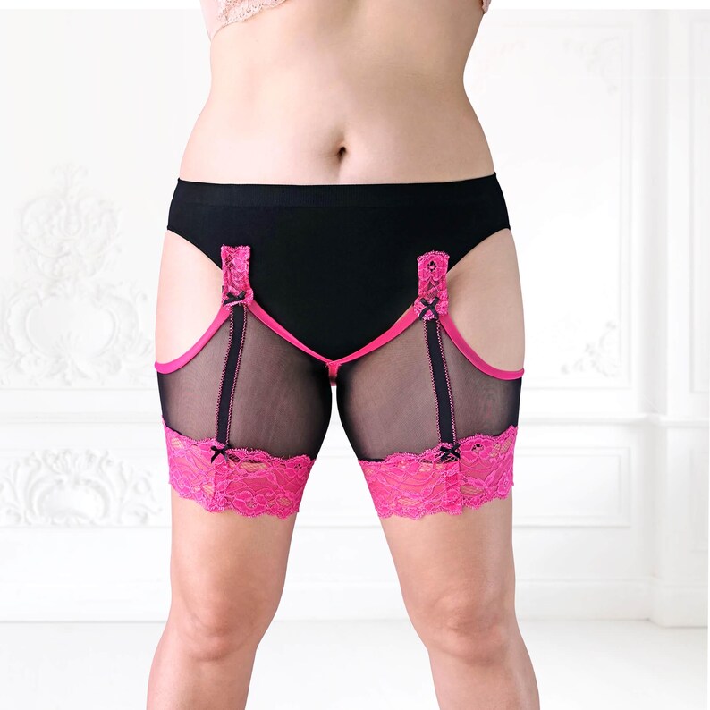 Front-facing image of model in wide stance wearing black mesh anti-chafing thigh bands with pink lace trim. Designed for chub rub protection.