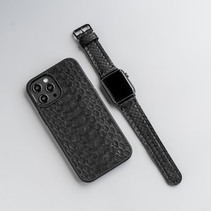 Op de afbeelding: Een zwarte leren telefoonhoes met een slangenhuidpatroon en een zwarte leren horlogeband met een zwarte wijzerplaat.