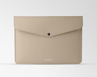 Puede incluir: Un clutch de sobre de cuero beige con un cierre de presión y el texto "F.P.K." grabado en la parte delantera.