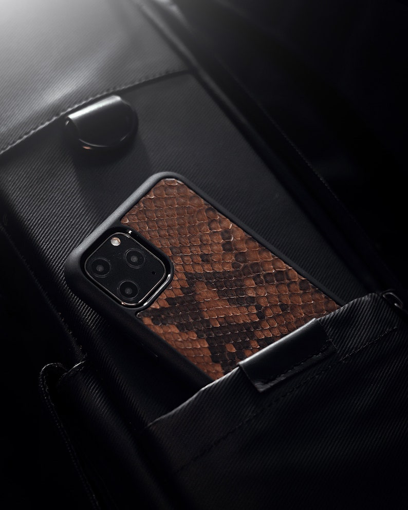 May include: A brown snakeskin phone case with a black camera lens cutout. The case is in a black bag.