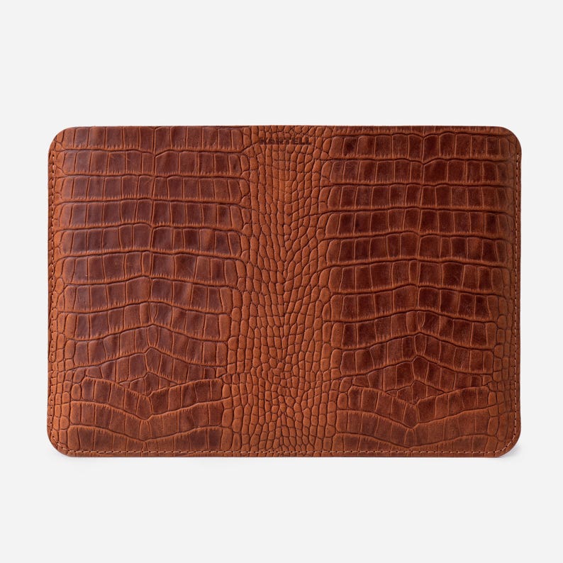 May include: A brown leather laptop sleeve with a crocodile-embossed pattern.