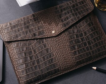 May include: A brown leather envelope with a crocodile pattern. The envelope has a flap with a gold button closure.