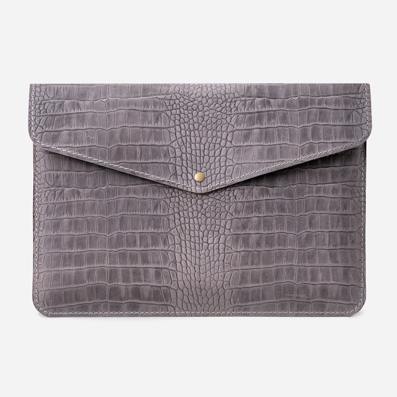 May include: A gray leather laptop sleeve with a crocodile embossed pattern and a gold button closure.