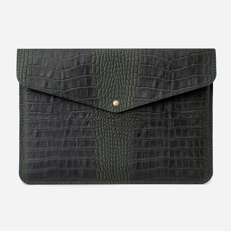 May include: A dark green leather laptop sleeve with a crocodile embossed pattern and a gold button closure.